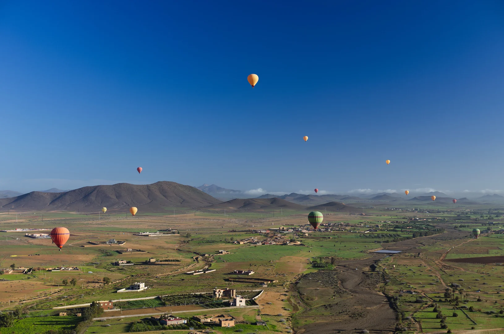 Vogelperspectief op groene palmboomtuinen en rode aarde vanuit een luchtballon bij Marrakech